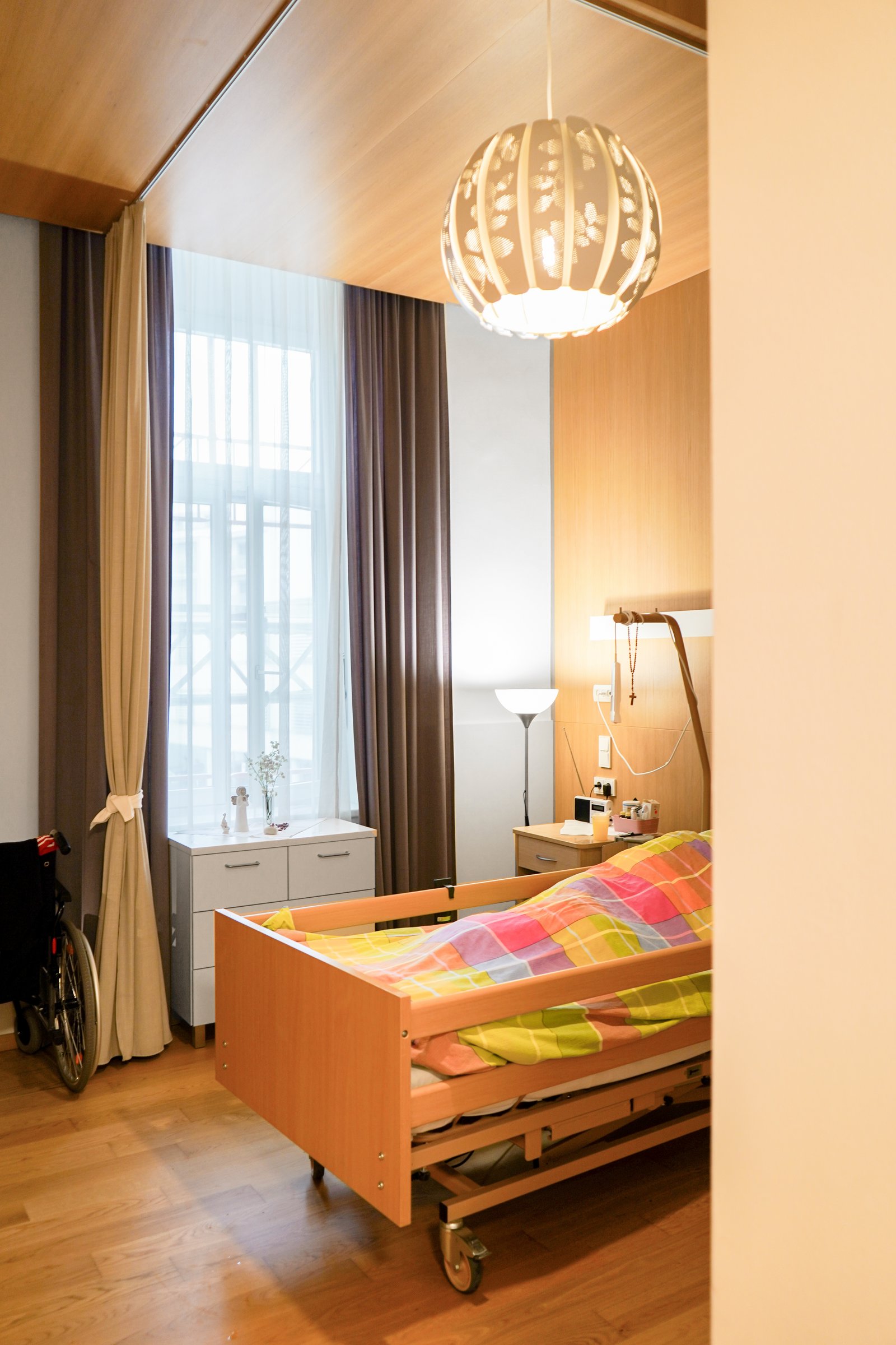 Gemütliches Zimmer mit Krankenbett, Vorhängen und Luster